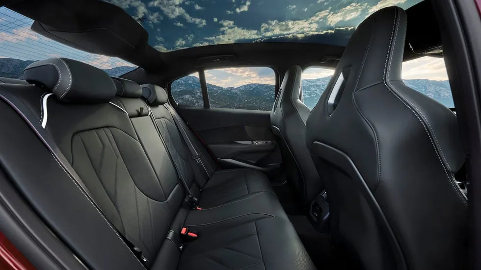 Interior view of a car's back seat with leather upholstery and a panoramic roof showcasing a scenic background.