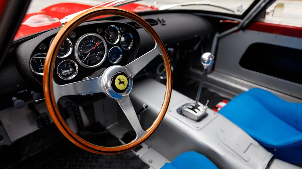vehicle interior view. Wood steering wheel, analog gauges, metal shifter and blue bucket seats.
