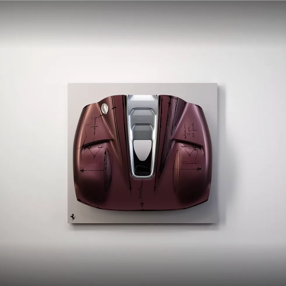 Ferrari car design model displayed on a wall with technical sketches and a sleek maroon finish.