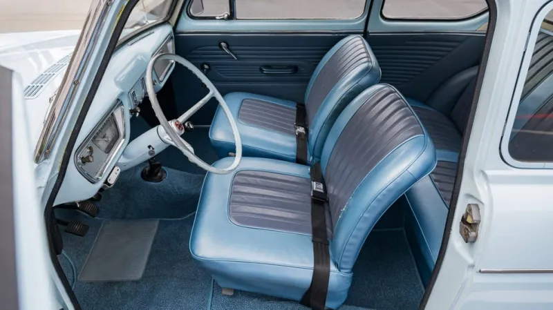 vehicle interior view, light blue vintage car cabin with blue seats, manual shifter and thin steering wheel.
