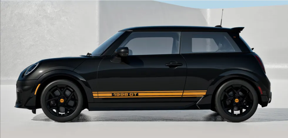 Паркованный чёрный Mini Cooper 1499 GT расположен у металлической конструкции с яркими жёлтыми боковыми полосами.