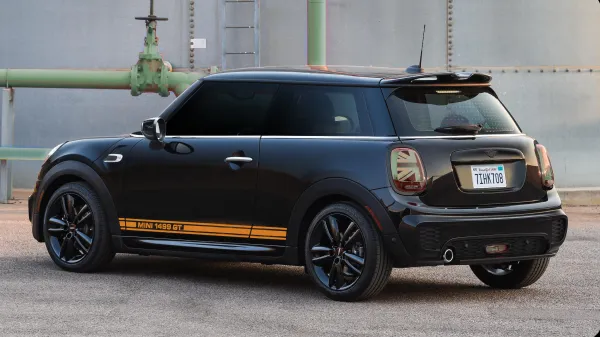 Black Mini Cooper 1499 GT parked beside a metallic structure with distinctive yellow stripes on the side.