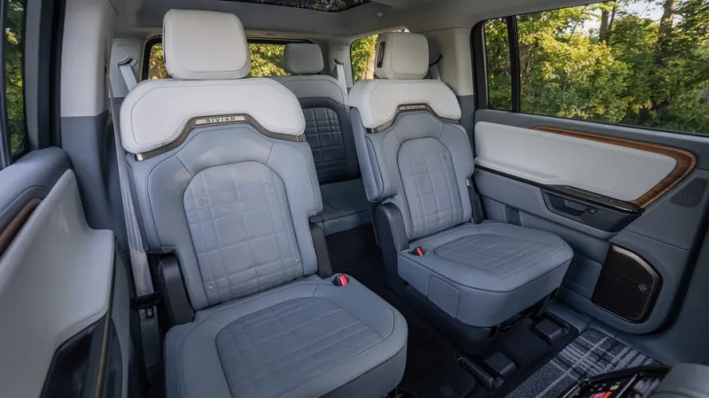 Серебряный SUV Rivian припаркован на улице с растительностью на фоне