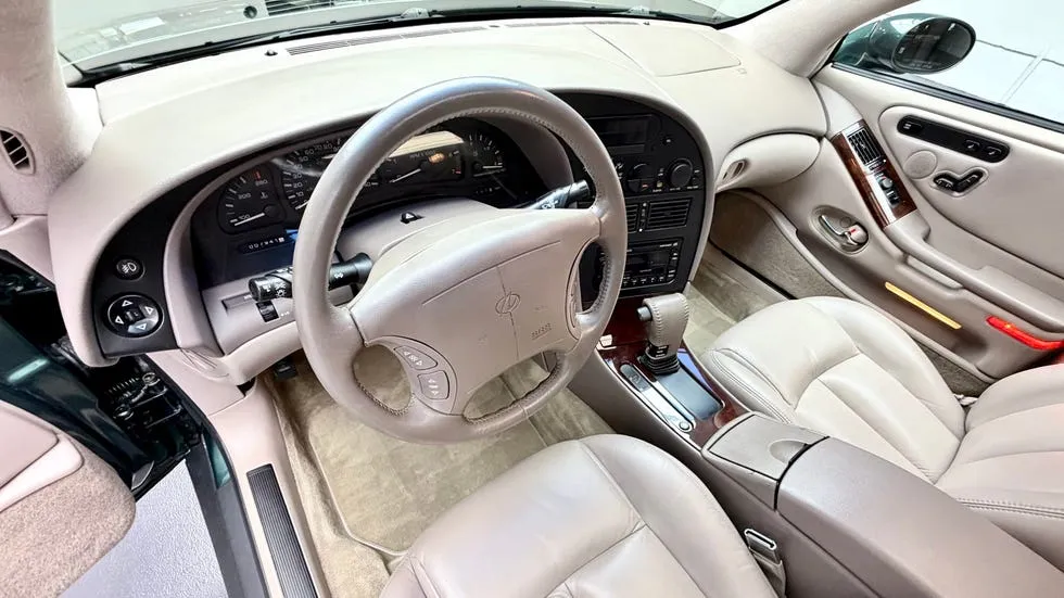 vehicle interior view. Beige leather cabin with wood trim, automatic shifter and clean dashboard.