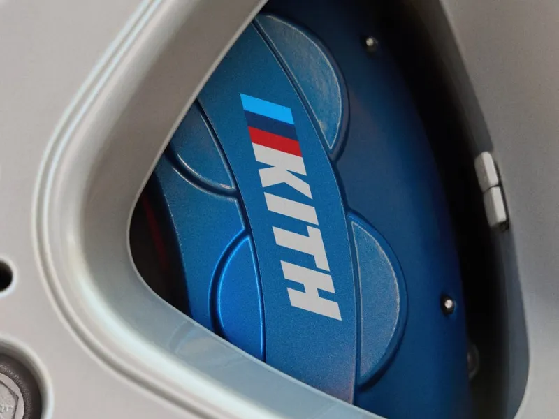 Close-up of a car wheel with a blue brake caliper featuring the "KITH" logo.